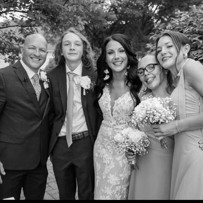 A bride beaming with her family and bridesmaids, bouquets in hand